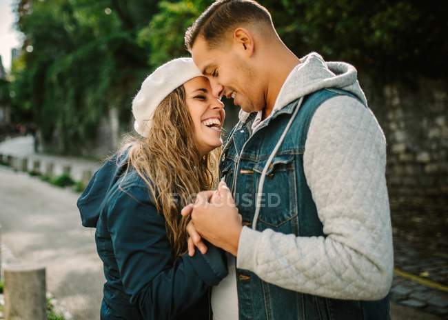 Content woman in casual clothing cuddling with pleased man in street, green plants on blurred background — Stock Photo