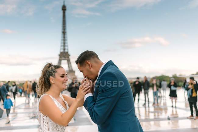 Groom en costume bleu et mariée en robe de mariée blanche baisers main avec Tour Eiffel sur fond à Paris — Photo de stock