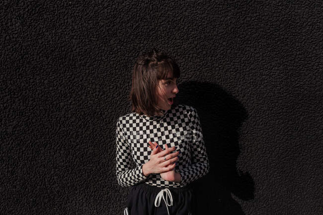 Elegante Teenagerin in stylischer schwarz-weiß karierter Jacke vor modernem Gebäude mit Blick auf die Stadtstraße — Stockfoto