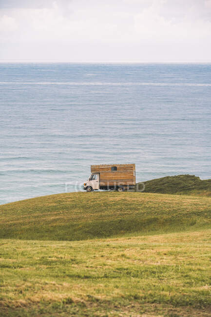 Goldenes Feld auf einem Hügel und kleiner Lastkraftwagen mit blauem Meer und bewölktem Himmel im Hintergrund bei Comillas Cantabria in Spanien — Stockfoto