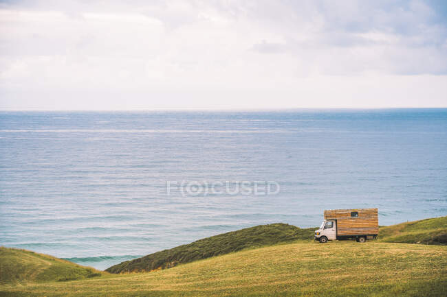 Goldenes Feld auf einem Hügel und kleiner Lastkraftwagen mit blauem Meer und bewölktem Himmel im Hintergrund bei Comillas Cantabria in Spanien — Stockfoto