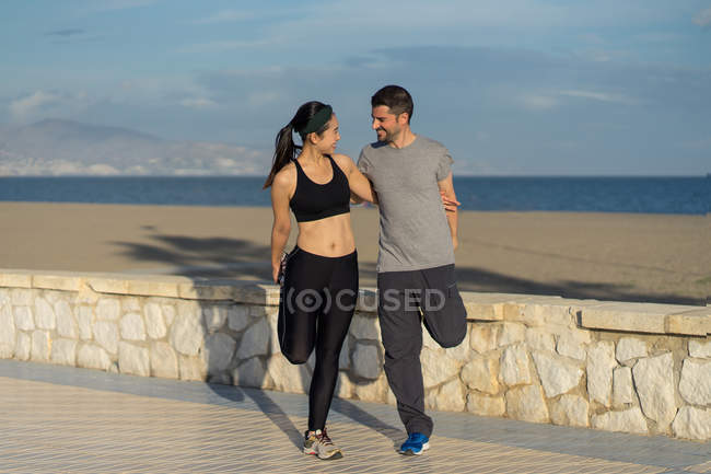 Coppia in piedi in una gamba mentre si tiene l'un l'altro in abbigliamento sportivo con mare blu e cielo su sfondo sfocato — Foto stock