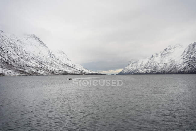 Tranquil lake against snowy hills in cold overcast weather — Stock Photo