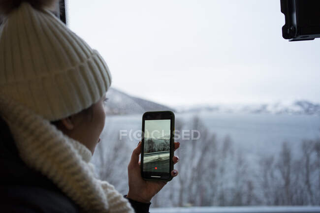 Mulher calma gravação de vídeo com smartphone de cenário wintry enquanto olha para fora da janela — Fotografia de Stock