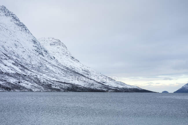 Tranquilo lago contra colinas nevadas en clima frío nublado - foto de stock