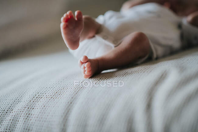 Pequeños pies de recién nacido en traje de cuerpo blanco descansando en cuna sobre fondo borroso - foto de stock