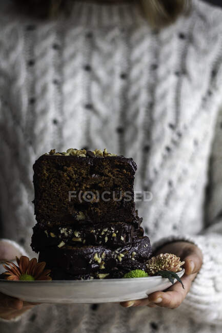 Unrecognizable female in sweater carrying plate with pieces of yummy banana bread and fresh flowers — Stock Photo