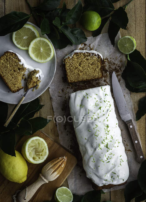 Top view of loaf of delicious pastry with sweet icing placed on wooden table near kitchenware and ripe lemons and limes — Stock Photo