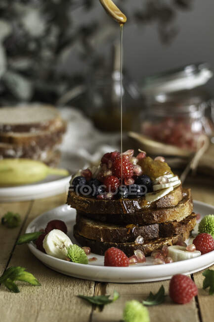 Miele liquido versato su una pila di pane tostato fresco con bacche fresche e menta durante la colazione in tavola — Foto stock