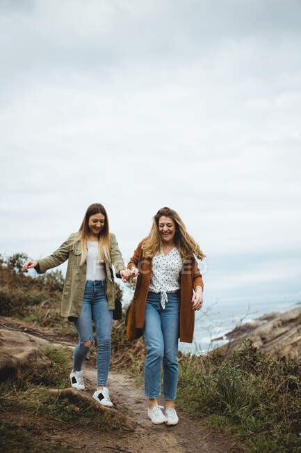 Amigos felizes do sexo feminino andando na trilha à beira-mar — Fotografia de Stock