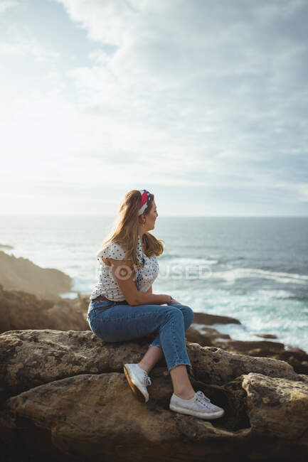 Mujer pensativa sentada en piedra y mirando el paisaje marino - foto de stock