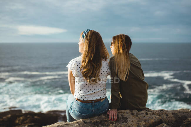 Мечтающие женщины, сидящие вместе на берегу и наслаждающиеся восходом солнца — стоковое фото