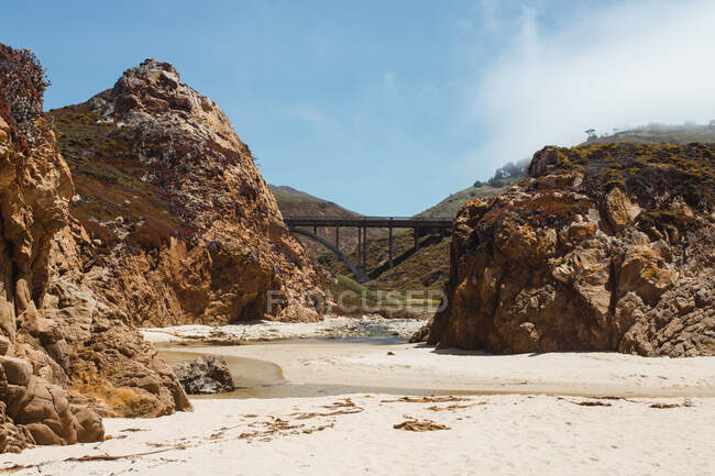 Vuoto spiaggia rocciosa sassosa e ponte sotto il cielo nuvoloso luce in Big — Foto stock
