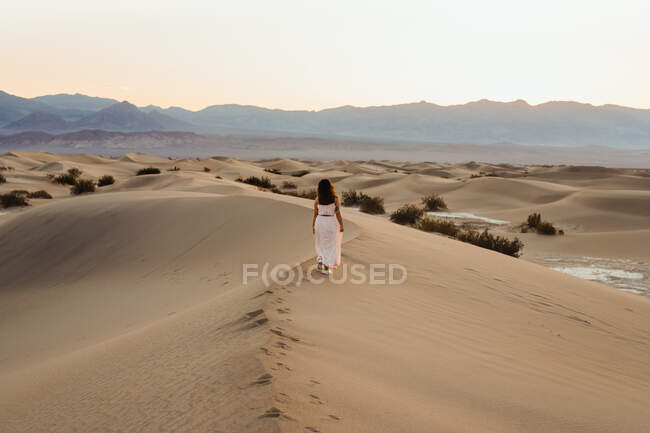 Обратный вид на молодую женщину, идущую по пустыне, оставляющую следы в — стоковое фото