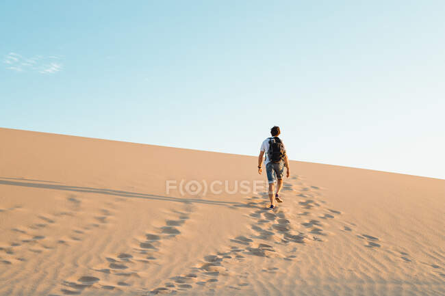 Самотній чоловік з рюкзаком, що йде в піщаній пустелі — стокове фото