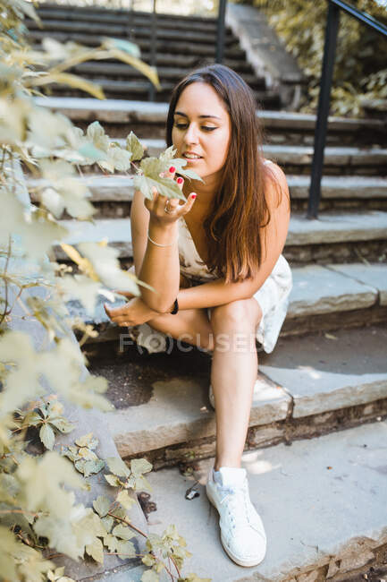 Stylish woman sitting on stairs of park in New York smelling flo — Stock Photo
