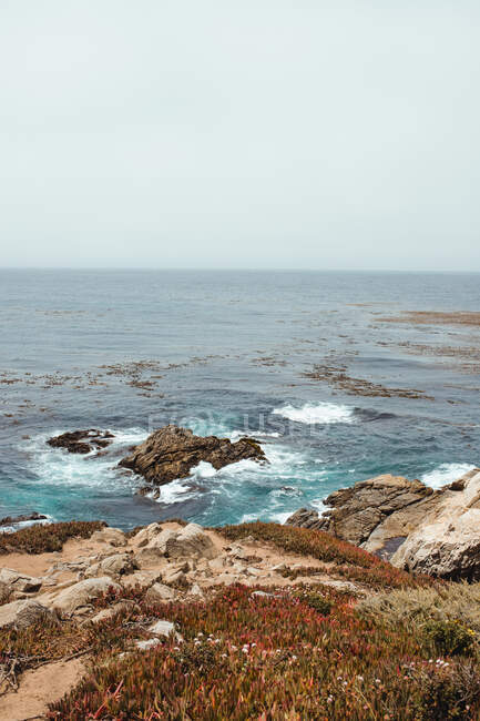 Blaue Wellen spülen bei hellem Tag felsige Meeresküste — Stockfoto