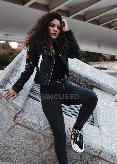Современная женщина в черной куртке и джинсах стоит в городе — стоковое фото