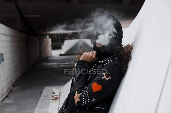 Femme en masque noir et veste fumant dans la rue — Photo de stock