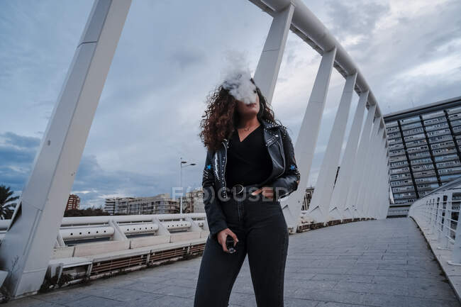 Elegante donna in giacca nera e jeans fumatori sul ponte — Foto stock
