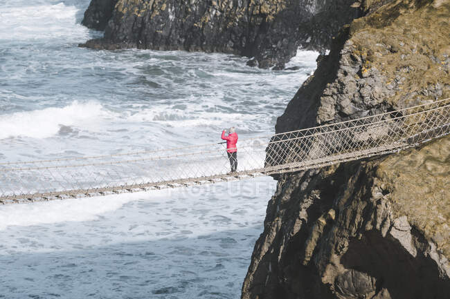 Tourist walking on rope bridge suspended between cliffs in North — Stock Photo