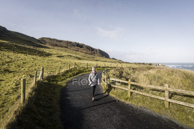 Woman walking on country road between sea and field — Stock Photo