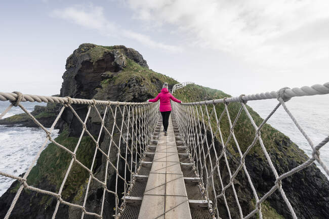 Woman crossing rope bridge leading to rocky island — Stock Photo
