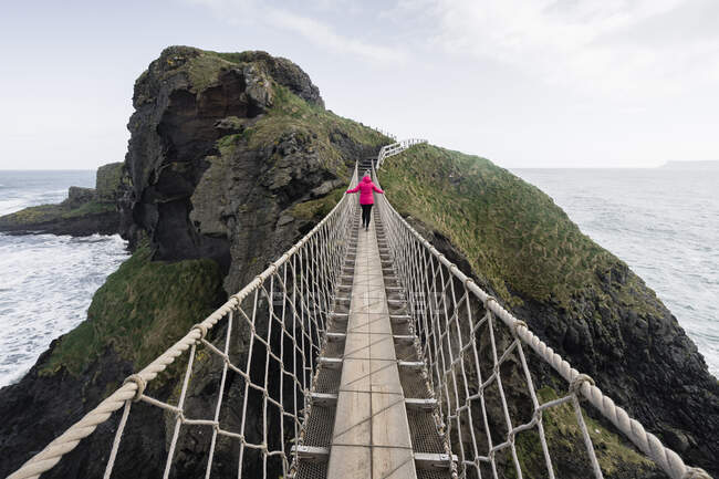 Donna che attraversa il ponte di corda che conduce all'isola rocciosa — Foto stock