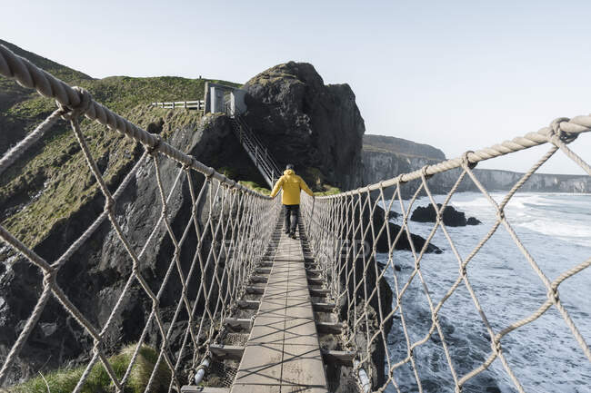 Man crossing rope bridge leading to rocky island — Stock Photo