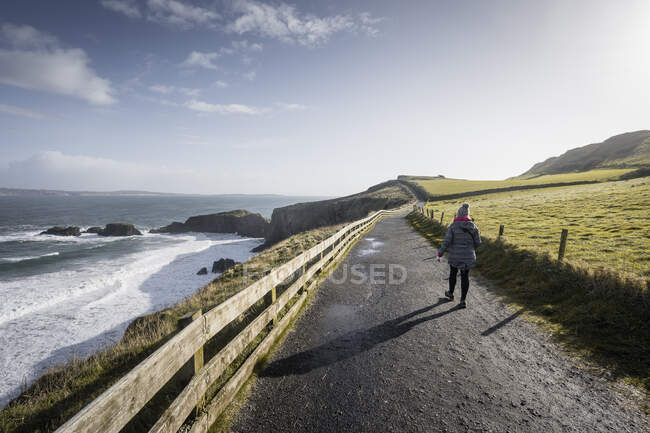 Person walking on country road between sea and field — Stock Photo