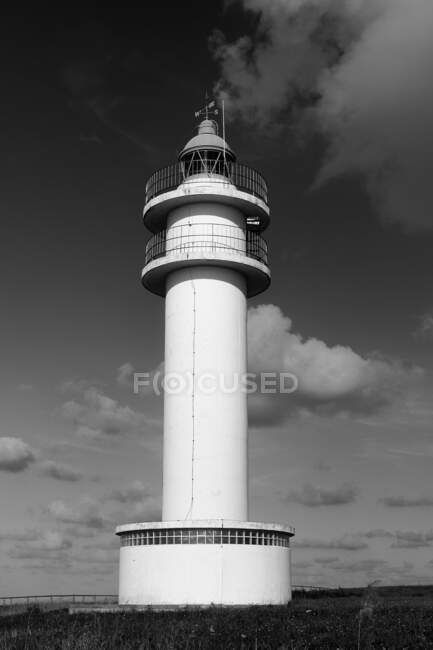Черно-белый старый маяк на лугу возле береговой линии в облачный летний день — стоковое фото