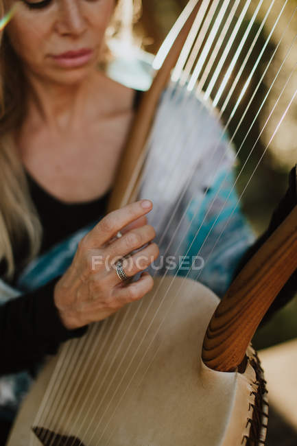 Romantic charming woman with blond hair enjoying melody while playing musical instrument and sitting in garden in summer — Stock Photo