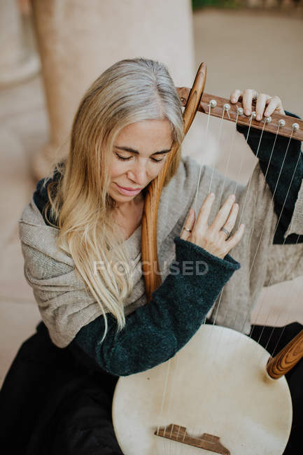 Dall'alto ispirato affascinante donna con i capelli biondi godendo la musica durante la riproduzione di strumenti musicali a corda in terrazza — Foto stock