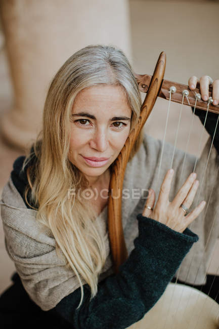 Desde arriba inspirada encantadora mujer con cabello rubio disfrutando de la música mientras toca el instrumento de cuerda musical en la terraza - foto de stock