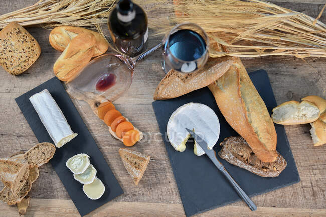 Von oben schmackhafte hausgemachte Scheiben Weißkäse und frisches, knuspriges Brot mit Flasche und Glas Rotwein auf rustikalem Holztisch — Stockfoto