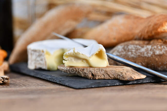 Восхитительные различные виды белого сыра и хрустящий свежий хлеб с кусками дерева на деревенском столе — стоковое фото