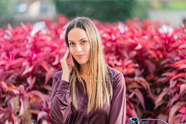 Уверенная длинноволосая деловая женщина в стильной фиолетовой блузке звонит по мобильному телефону — стоковое фото