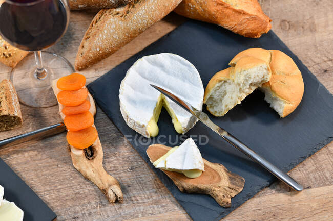 Зверху смачні домашні скибочки білого сиру і свіжий хліб з пляшкою і склянкою червоного вина на сільському дерев'яному столі — стокове фото