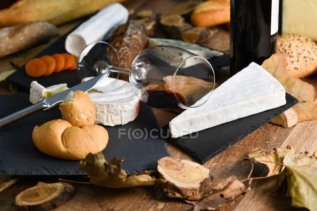Tasty homemade slices of white cheese and fresh crusty bread with bottle and glass of red wine on rustic wooden table — Stock Photo