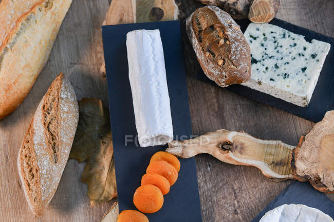 From above delightful various types of white cheese and crispy fresh bread with pieces of wood on rustic table — Stock Photo