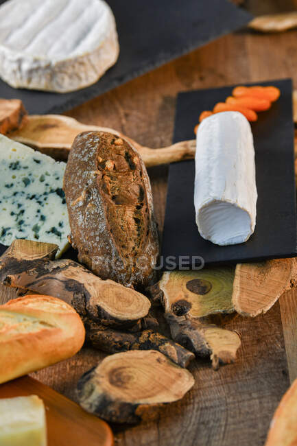 Köstliche Weißkäsesorten und knuspriges frisches Brot mit Holzstücken auf rustikalem Tisch — Stockfoto