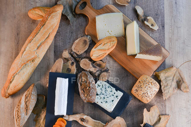 From above delightful various types of white cheese and crispy fresh bread with pieces of wood on rustic table — Stock Photo