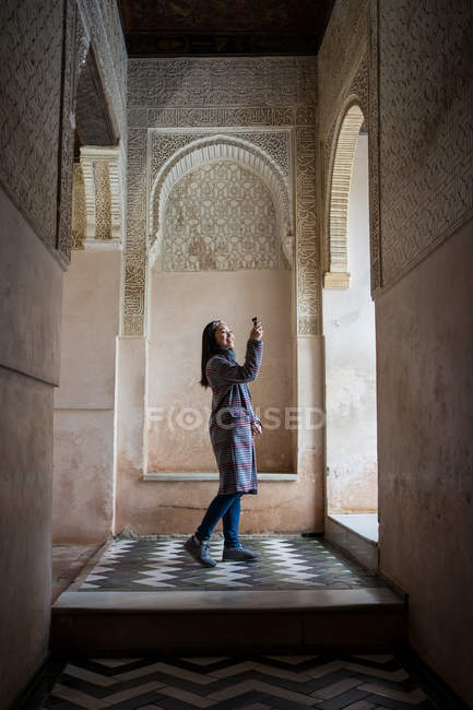 Turista ammirando ornamento sopra finestra ad arco all'interno di antico palazzo islamico scattando foto con piccolo dispositivo fotocamera — Foto stock