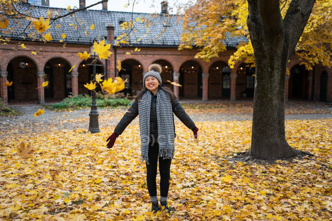 Fröhliche Asiatin wirft im Innenhof der Osloer Kathedrale in Norwegen gelbe Ahornblätter — Stockfoto
