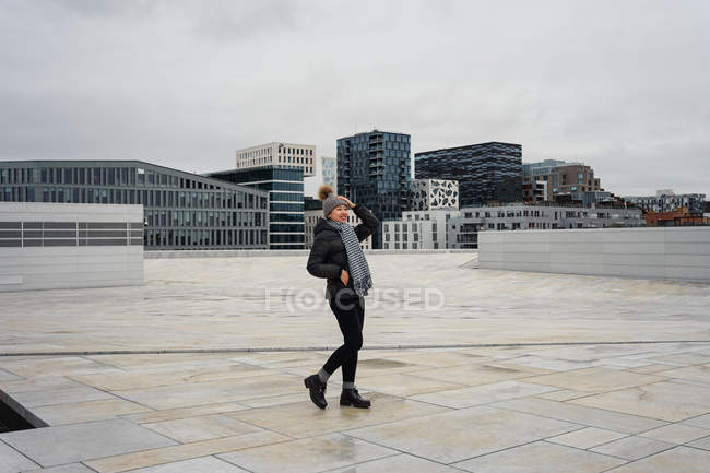 Cheerful young woman wearing winter clothes and standing on plaza at Oslo Opera House — Stock Photo