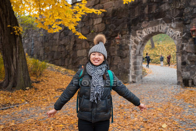 Jovem asiática alegre jogando folhas amarelas de bordo enquanto está em pé no pátio da Catedral de Oslo na Noruega — Fotografia de Stock