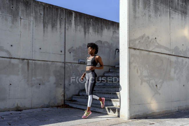 Atlético Africano mulher americana em esportes top e leggings correr para baixo escadas durante o treinamento em dia de verão ensolarado na cidade — Fotografia de Stock