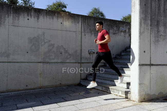 Мужчина в красной рубашке и черных штанах бегает по лестнице во время тренировки в солнечный летний день в городе — стоковое фото