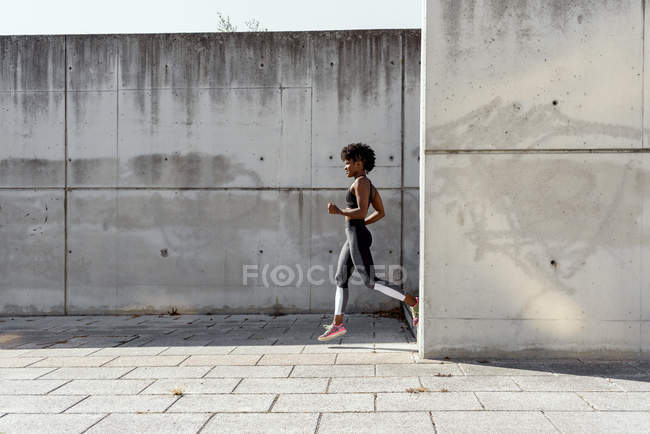Atletismo mujer afroamericana en la cima de los deportes y los leggings que bajan las escaleras mientras entrena en soleado día de verano en la ciudad. - foto de stock