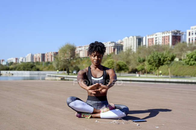 Афроамериканська жінка на спортивному вершку і лаки сидять у позі лотоса і розтягують руки вгору під час відпочинку. — стокове фото